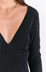 Close-up of the deep V-neckline and shoulder of a black polka dot long sleeve dress