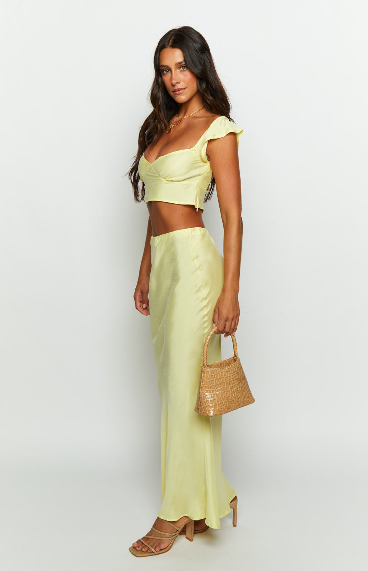 Side view of a pale yellow satin maxi skirt with a fitted high waist and a flowing A-line silhouette