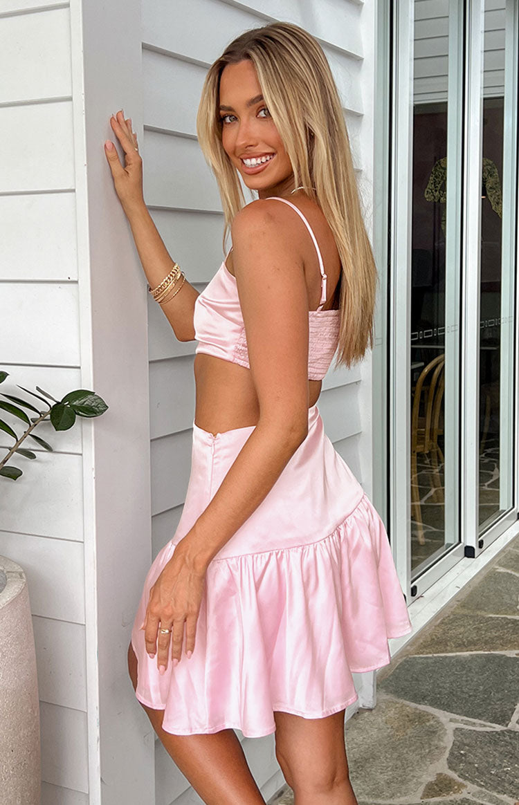 Side view of a pink satin mini dress showing the smocked back, side cutout, and ruffled hem