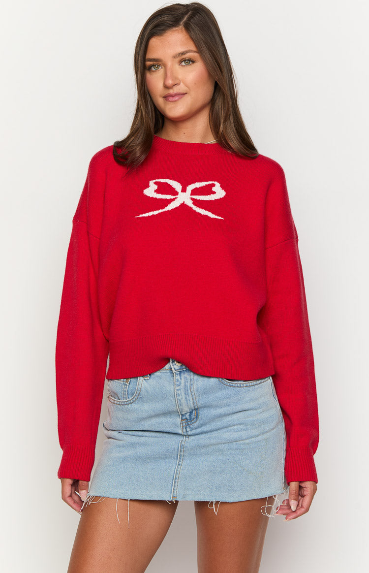 Front view of a red knit sweater with a white knitted bow graphic on the chest and ribbed cuffs and hem