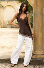 Brown satin asymmetrical top with lace trim on the V-neckline and hem, featuring thin spaghetti straps and a flowy fit