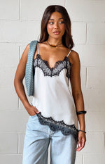White satin asymmetrical top with black lace V-neck and detailed scalloped lace trim on the asymmetrical hem