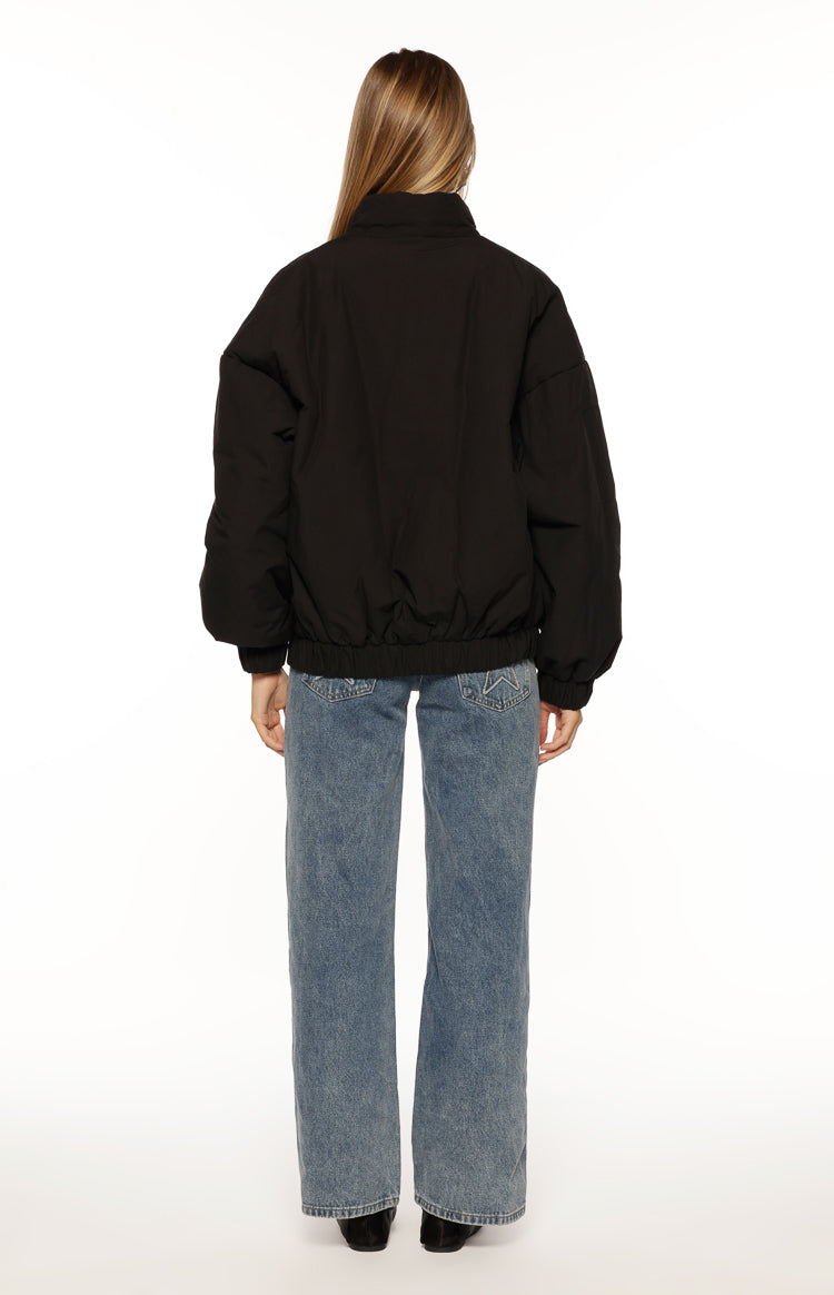 Rear view of a black oversized puffer jacket with a high collar, voluminous sleeves, and elasticated hem and cuffs