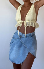 Light blue denim mini skirt with an asymmetrical wrap front, V-shaped waist, and single button closure
