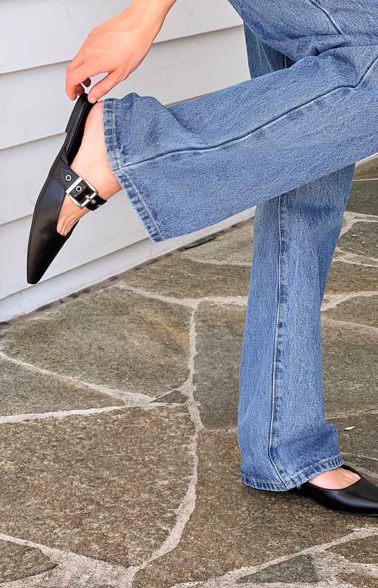 Side view of black pointed-toe mules with a decorative silver buckle strap across the top of the foot