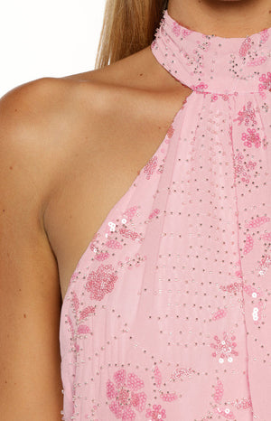 A close up vertical image focusing on the neckline and shoulder of a pink mini dress. The dress features a high gathered halter neck and is embellished all over with small silver beads and larger pink sequins arranged in a floral pattern.