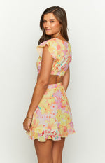 Side view showing the back zipper, cut-out waist, flutter sleeves, and ruffled hem of a yellow floral mini dress