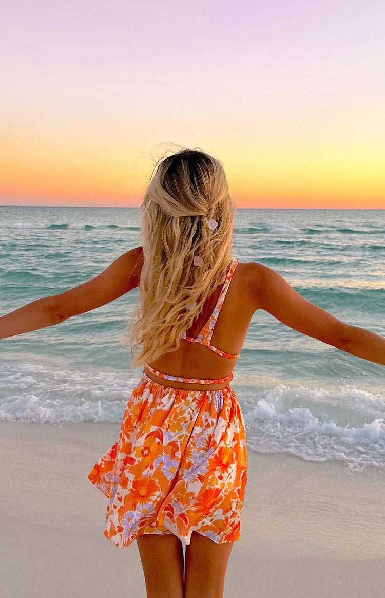 Side view of an orange floral mini dress showing the deep V-neck, side cutouts, and tie-back detail