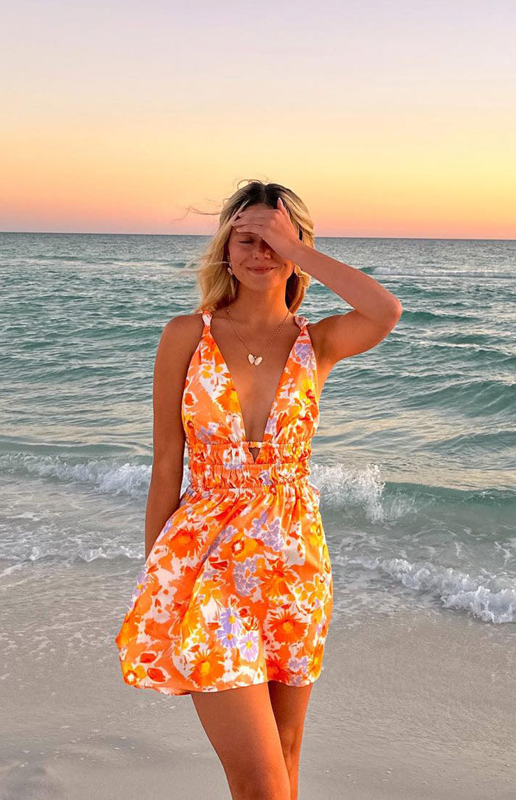 Front view of an orange floral mini dress with a deep V-neck, tied shoulder straps, and a ruched elasticated waist