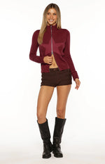 Front view of a cropped burgundy knit zip-up sweater with a high neck, large lighter star design, and partially open zipper
