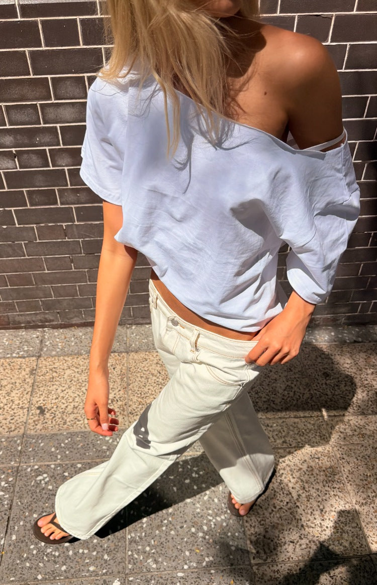 White off shoulder boxy tee with a relaxed fit and short sleeves, draped loosely over one shoulder