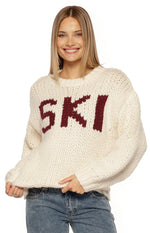 Front view of a cream chunky knit sweater with burgundy "SKI" jacquard lettering and ribbed cuffs