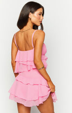 Side-rear view of a pink mini dress featuring multiple tiers of ruffles on the top and skirt, with thin adjustable spaghetti straps