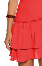 A close-up shot focusing on the skirt of a red mini-dress. The skirt features two tiered ruffles made of a lightweight fabric. The top ruffle has subtle gathering and slight frill detailing where it attaches to the fitted section of the dress.