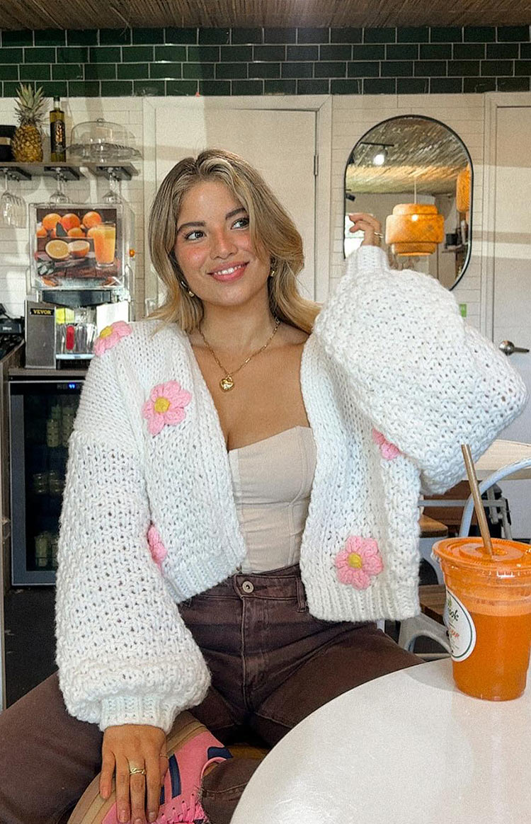 Close-up of the chunky white open knit cardigan with pink and yellow flower appliques on the sleeves