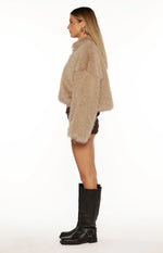 Side view of a light brown faux fur jacket with a cropped length and long sleeves