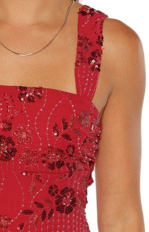 A close-up of the bodice of a red mini dress. The fabric is heavily embellished with an intricate dense pattern of red sequins forming floral shapes and fine silver beaded details outlining and connecting the design. This mini features a square neckline and a wide embellished strap over the shoulder.