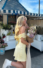 Side view of a primrose yellow satin mini dress with ruched off-shoulder sleeves and a tie-back