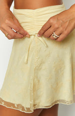 Detail shot of the yellow mesh mini skirt's ruched drawstring waist and delicate floral lace pattern