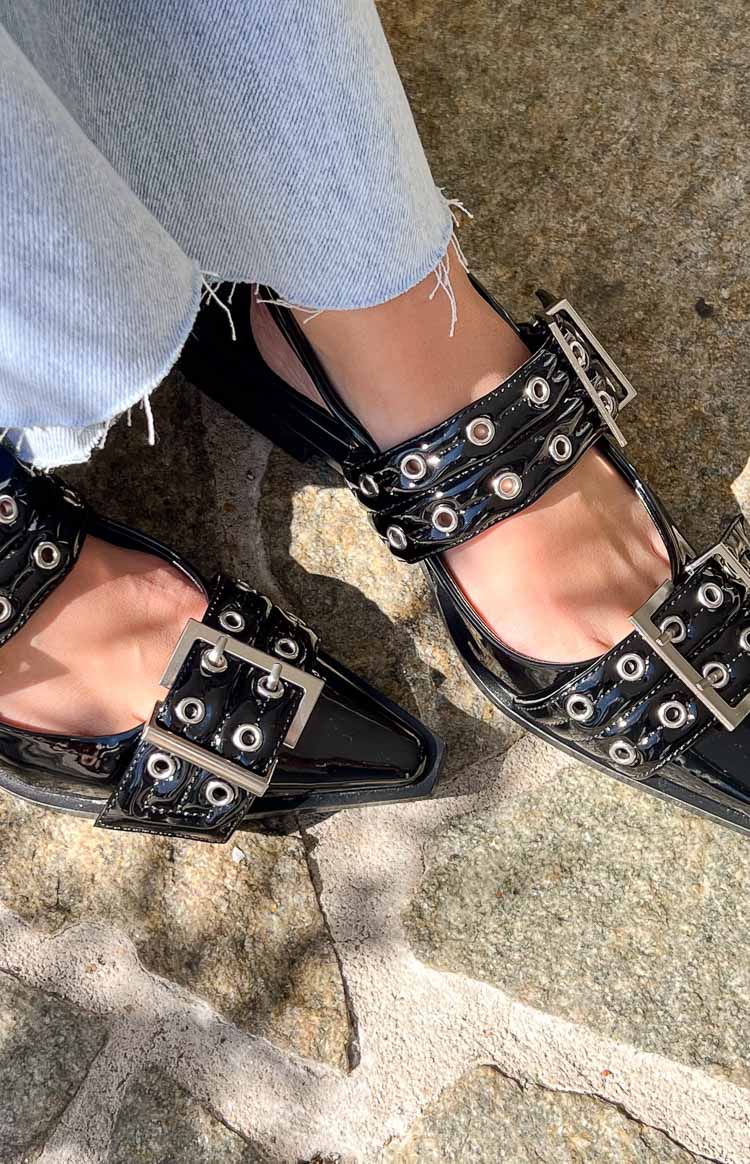 Close-up of the black patent pointed flats with two buckled straps adorned with silver eyelets