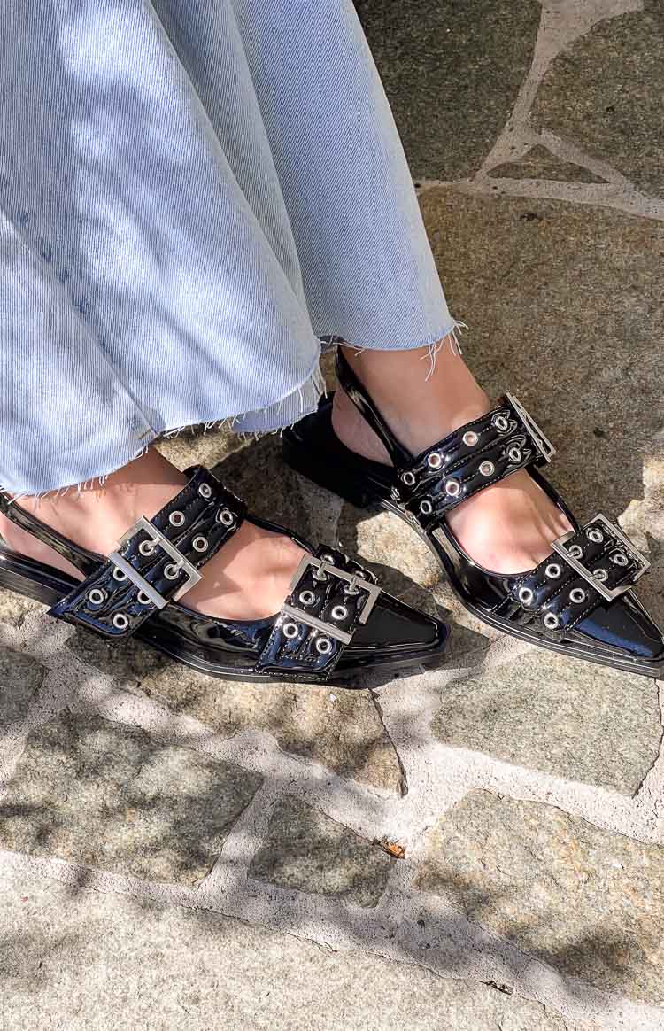 Black patent pointed flats with two buckled straps featuring silver eyelets and a slingback design